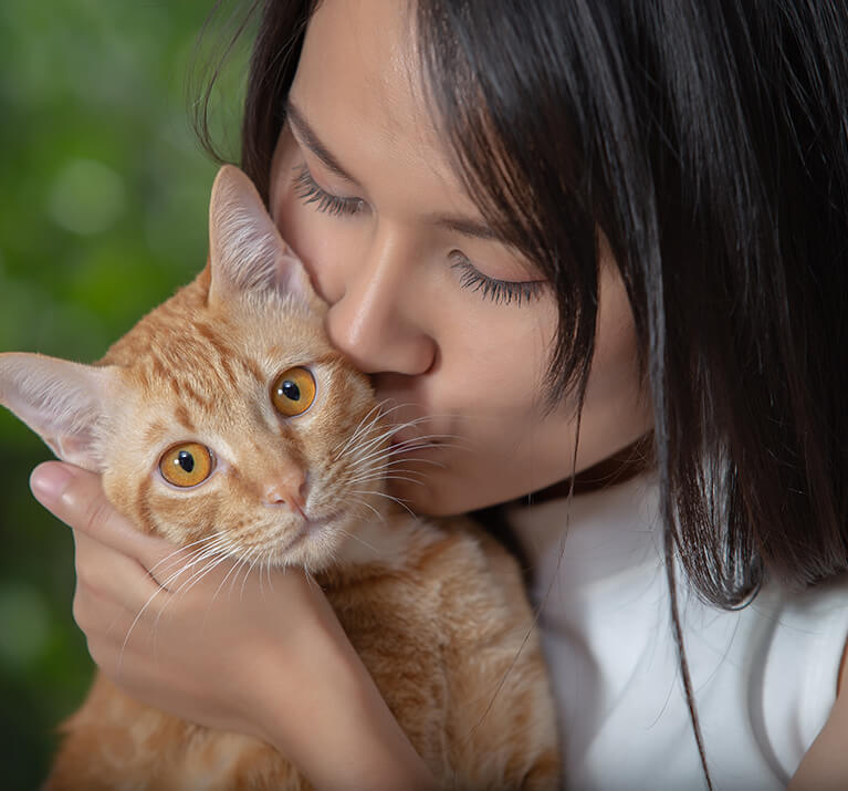 Une jeune femme embrasse un chat roux tigré sur la joue.